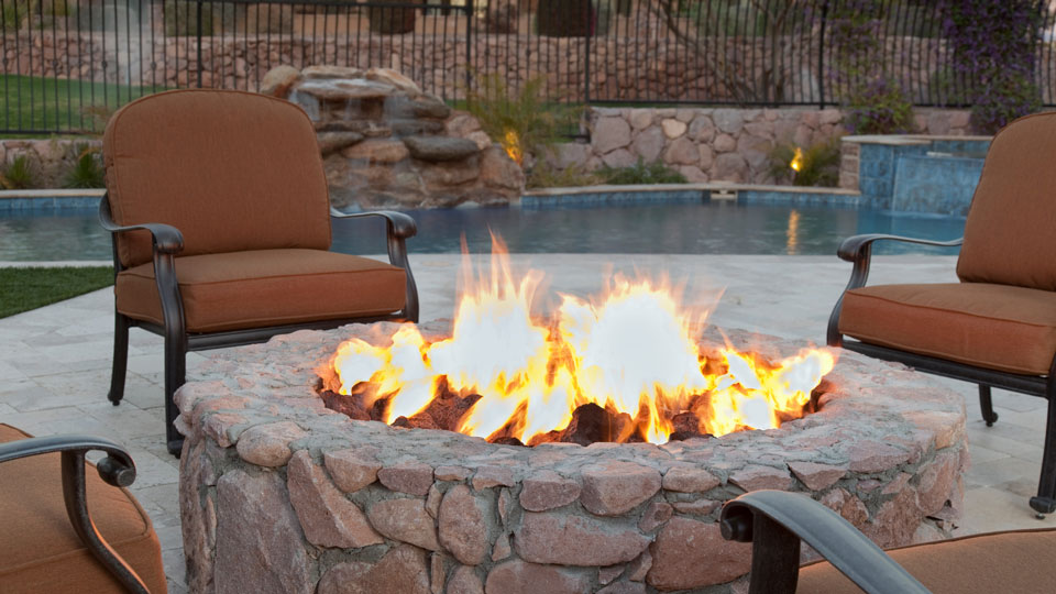 Eine Feuerstelle auf einer Terrasse mit einem Pool im Hintergrund.