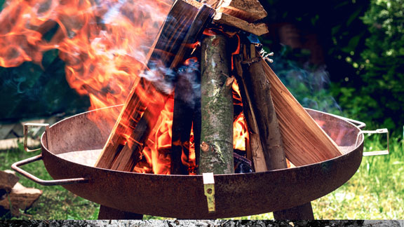 Man sieht eine Feuerschale, in der Holz brennt.