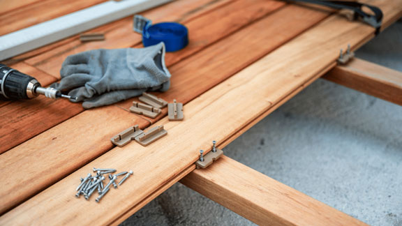 Schrauben, Handschuhe und andere Werkzeuge, welche auf Holzbrettern liegen. 