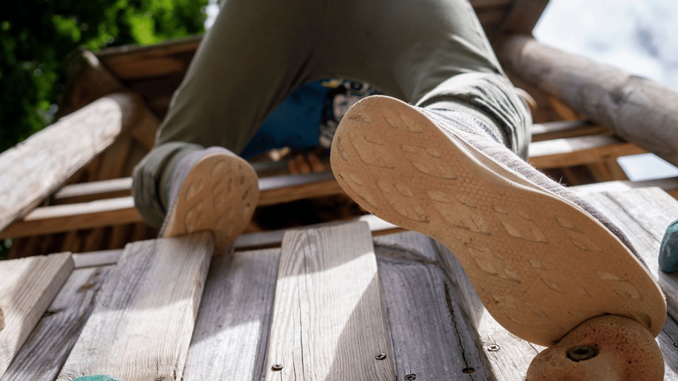 Ein Mensch, der gerade ein Klettergerüst hochklettert. Man sieht seine Schuhe von unten. 