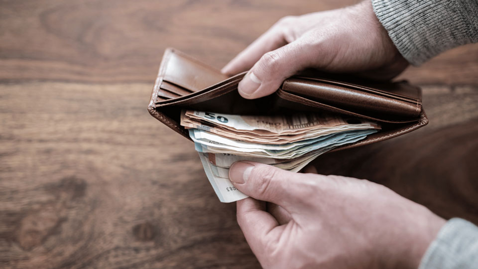 Das Bild zeigt eine Hand, die einen Geldbeutel mit mehreren Banknoten, darunter ein 50-Euro-Schein, öffnet.