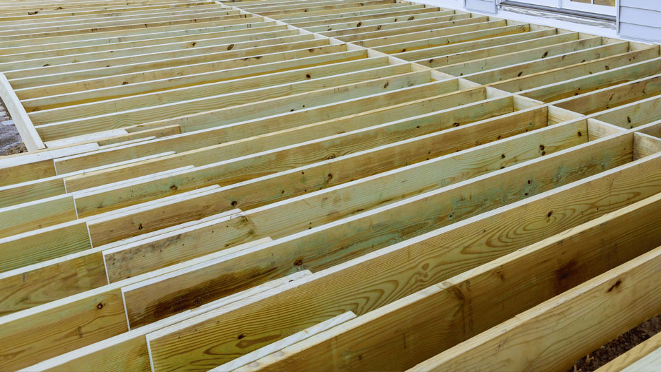 Das Bild zeigt eine Reihe von Holzlatten, die zu einem Fundament für eine Holzterrasse oder ein ähnliches Bauprojekt verlegt sind. Die Latten sind gleichmäßig angeordnet und die Struktur ist vorbereitet, um mit weiteren Baumaterialien fortzufahren.