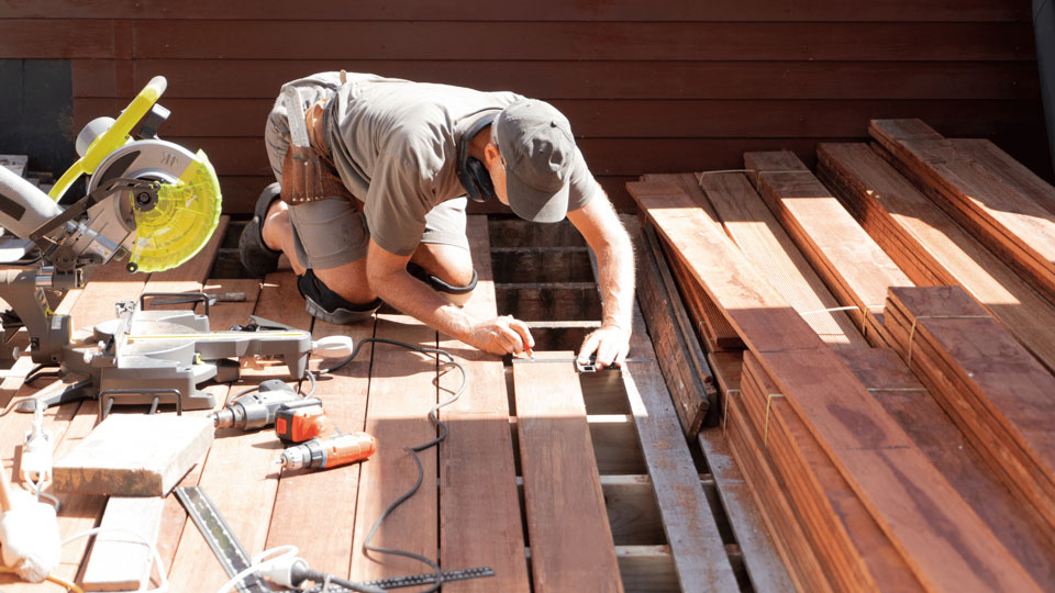 Ein Handwerker markiert Holzplanken auf einer Terrasse, um sie präzise zu verarbeiten.