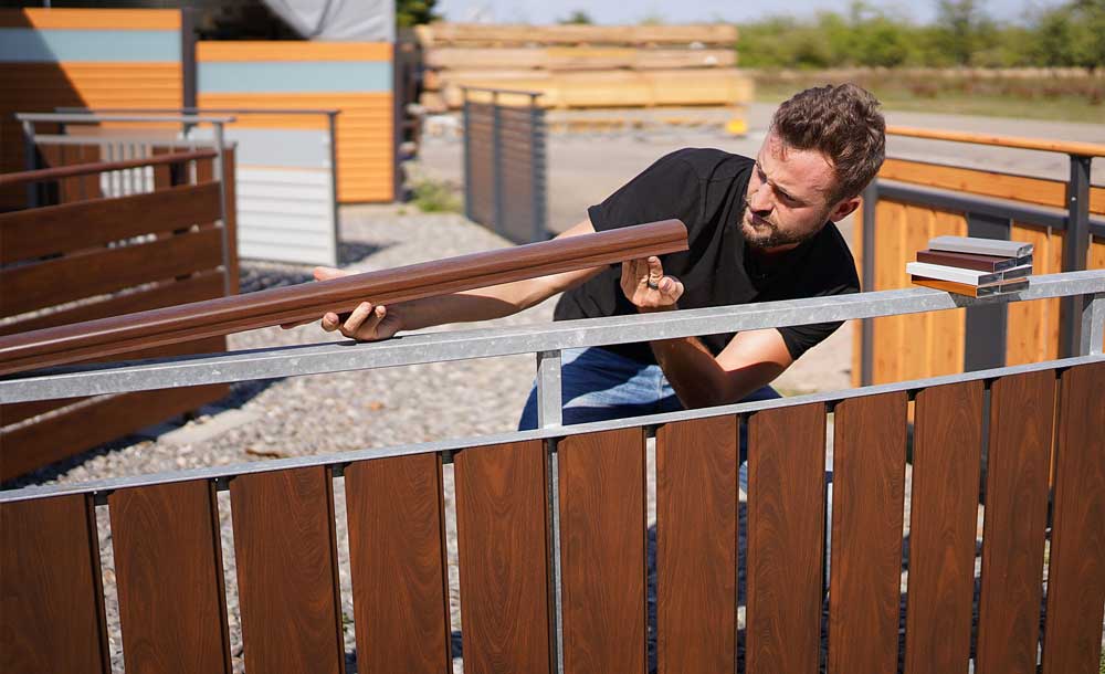 Alu Systeme Ausstellung in Neuried. Produktaustellung von Alupreisfux, einem Hersteller und Händler für Alu-Systeme in Neuried. Gérôme Birk (Inhaber) schaut sich ein Aluminiumprofil seines Alu-Balkongeländers an. Im Hintergrund sieht man Aluminium-Sichschutzzäune von Alupreisfux.